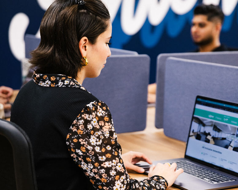 Woman working on laptop in shared workspace with privacy dividers.
