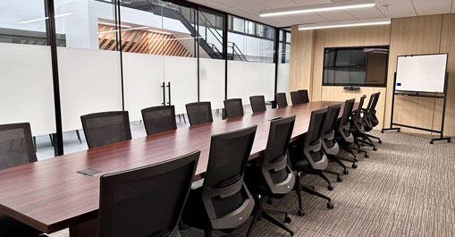 Long meeting table with mesh chairs and presentation screen in modern room.