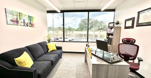 Private office with black sofa, desk, and window overlooking parking lot.