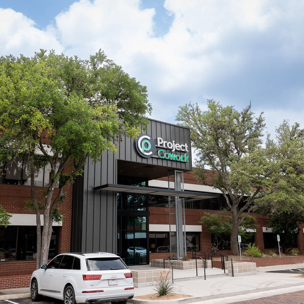 Exterior view of a building with “Project Cowork” signage and trees, captured under a clear sky.