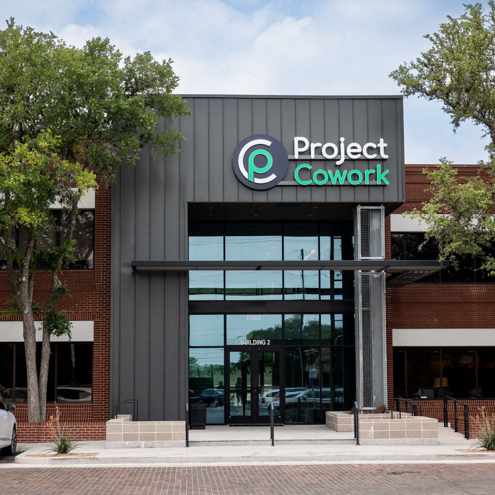 Exterior view of a building with “Project Cowork” signage and trees, captured under a clear sky.