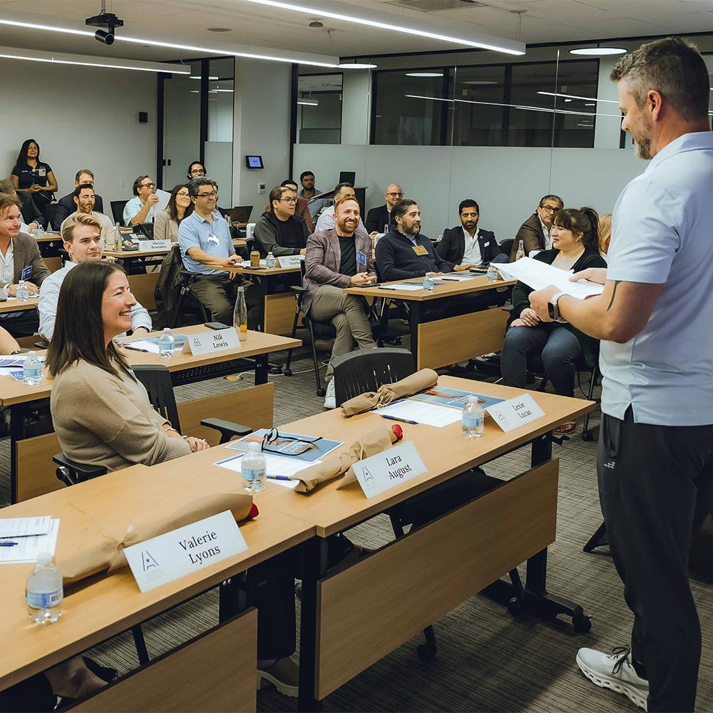 A large group of people sits in a Project Cowork training room and listens to a presentation