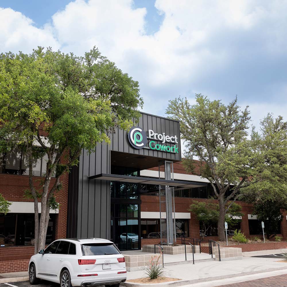 Exterior view of a building with “Project Cowork” signage and trees, captured under a clear sky.